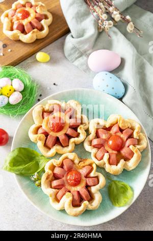 Ideal für Osterfrühstück oder -Mittagessen. Mini-Pizza. Pizza in Blätterteig mit Käse und Tomaten auf dem festlichen Tisch. Stockfoto