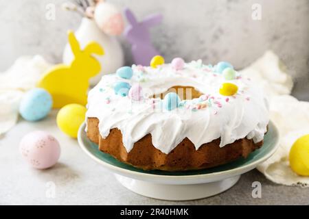 Glasierter osterzitronenkuchen mit Süßwaren und Mini-Schokoladeneiern auf grauem Steinhintergrund. Frohes Osterfest Stockfoto