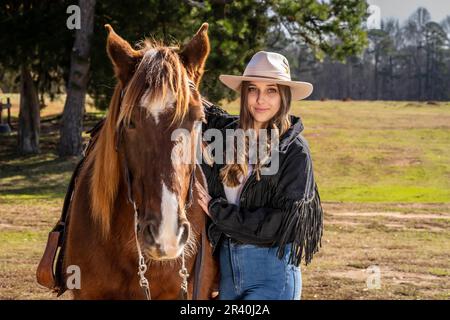 Ein wunderschönes braunes Cowgirl posiert mit ihrem Pferd, bevor es auf dem Land reitet Stockfoto