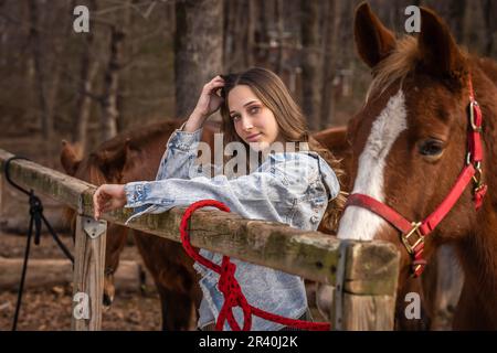 Hübsches braunes Cowgirl, das einen Tag mit ihrem Pferd auf der Farm genießt Stockfoto