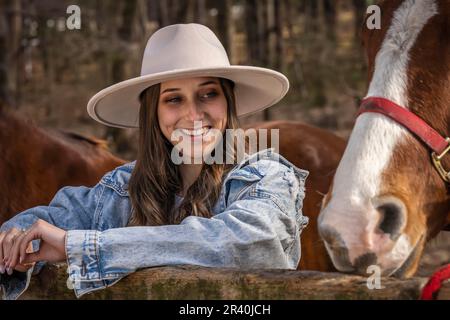 Hübsches braunes Cowgirl, das einen Tag mit ihrem Pferd auf der Farm genießt Stockfoto