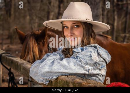 Hübsches braunes Cowgirl, das einen Tag mit ihrem Pferd auf der Farm genießt Stockfoto