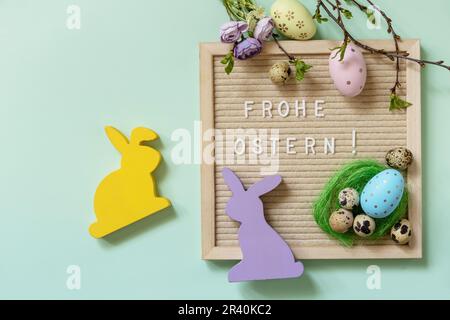 Brieftafel mit Frohe Ostern: Frohe Ostern in deutscher Begrüßung, Ostereier und grüne Zweige auf grünem Hintergrund. Ansicht von Stockfoto