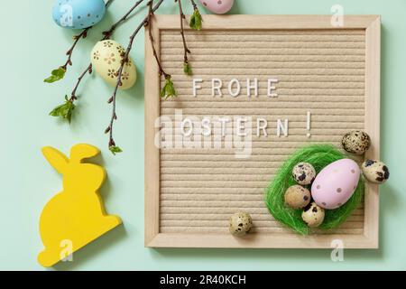 Brieftafel mit Frohe Ostern: Frohe Ostern in deutscher Begrüßung, Ostereier und grüne Zweige auf grünem Hintergrund. Ansicht von Stockfoto