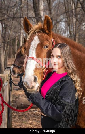 Hübsches braunes Cowgirl, das einen Tag mit ihrem Pferd auf der Farm genießt Stockfoto