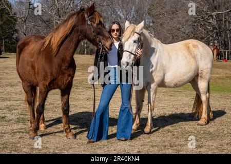 Hübsches braunes Cowgirl, das einen Tag mit ihrem Pferd auf der Farm genießt Stockfoto