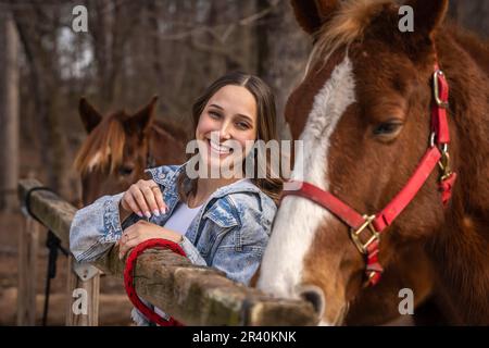 Hübsches braunes Cowgirl, das einen Tag mit ihrem Pferd auf der Farm genießt Stockfoto