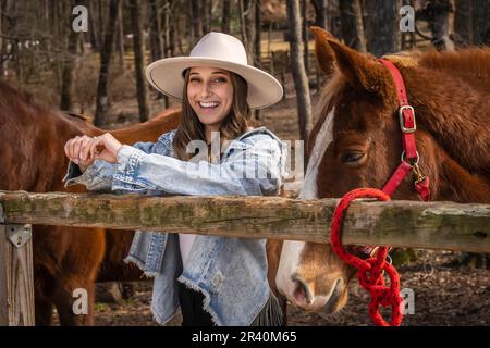 Hübsches braunes Cowgirl, das einen Tag mit ihrem Pferd auf der Farm genießt Stockfoto