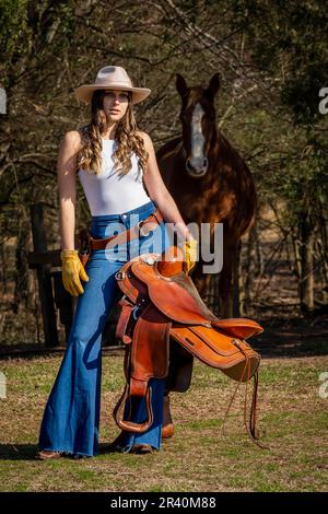 Hübsches braunes Cowgirl, das einen Tag mit ihrem Pferd auf der Farm genießt Stockfoto