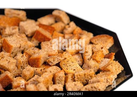 Getoastete Brotwürfel auf schwarzem Teller vor weißem Hintergrund Stockfoto