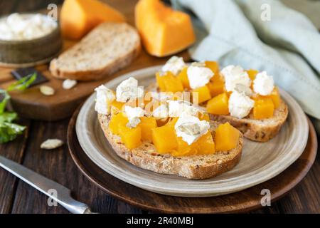 Gesundes Essen, vegetarische Vorspeise auf einem rustikalen Tisch. Offene Sandwiches vollkörniger Ciabatta mit Gewürzkürbis und Fetakäse. Stockfoto