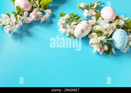 Osterkomposition mit bunten Eiern und Apfelblumen auf blauem Hintergrund. Frühlingskonzept, Blumenzusammensetzung. Grüß Dich Stockfoto