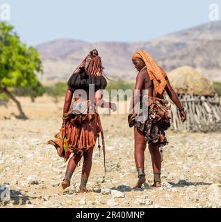 Zwei Frauen des Himba-Stammes laufen in Nationalkleidung durch die Wüste. Stockfoto