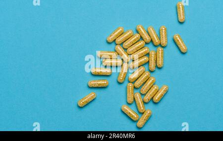 Transparente medizinische Kapseln mit gelbem Granulat innen auf blauem Hintergrund, Tabletten zur Behandlung, Vitamine Stockfoto