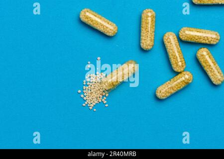 Transparente medizinische Kapseln mit gelbem Granulat innen auf blauem Hintergrund, Tabletten zur Behandlung, Vitamine Stockfoto