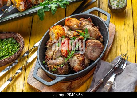 Grillfleisch - Schweinefleisch, Huhn und Gemüse auf einer gusseisernen Pfanne. Gegrillte Spieße auf gelbem Holzhintergrund. Draufsicht Stockfoto