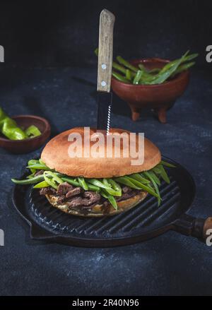Chilenischer lateinamerikanischer Sandwich-Burger Chacarero mit hochwertigen Rinderschnitten und grünen Bohnen auf schwarzem Hintergrund. Stockfoto