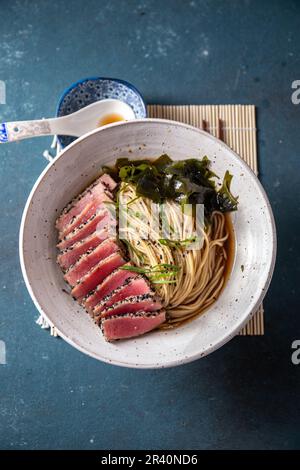 Thunfischsteak Ramen. Japanische Suppe mit Nudeln Ramen, Miso, gebratenem Thunfischsteak und Algen aus Algen. Draufsicht. Blauer Hintergrund. Stockfoto