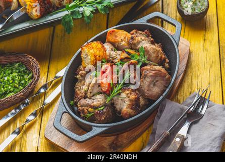 Grillfleisch - Schweinefleisch, Huhn und Gemüse auf einer gusseisernen Pfanne. Gegrillte Spieße auf gelbem Holzhintergrund. Draufsicht Stockfoto