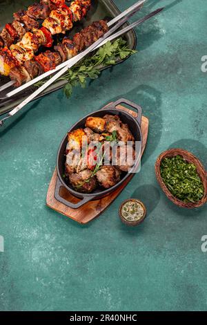 Grillfleisch - Schweinefleisch, Huhn und Gemüse auf einer gusseisernen Pfanne. Gegrillte Spieße auf gelbem Holzhintergrund. Draufsicht Stockfoto