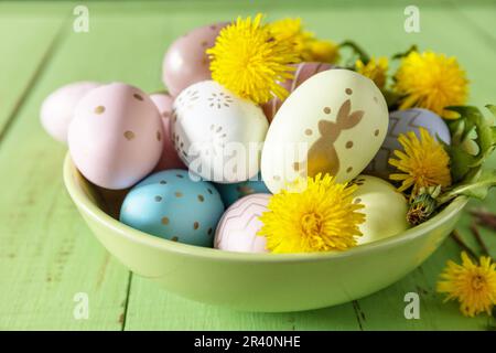 Frohe Osterferien. Handgemachte Ostereier und Frühlingsblumen Löwenzahn auf einem rustikalen Holztisch. Osterkomposition. Stockfoto