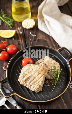 Gekochtes saftiges Thunfischsteak mit Gewürzen, Tomaten und Rosmarin auf einer Steinplatte. Essen im Restaurant. Meeresfrüchte. Rustikaler Stil. Stockfoto