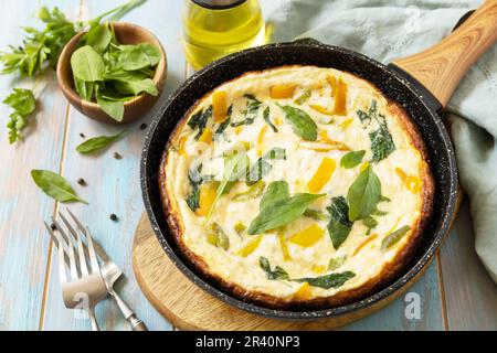 Gesundes Frittata oder gefülltes Omelett in der Pfanne auf rustikalem Holzhintergrund. Italienisches Omelette mit Bio-Spinat und Paprika. Stockfoto