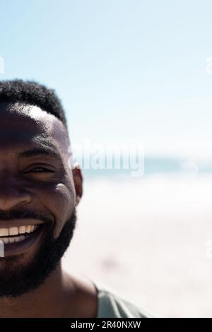 Gekürztes Gesicht eines bärtigen afroamerikanischen Mannes am Strand gegen Meer und klaren Himmel Stockfoto