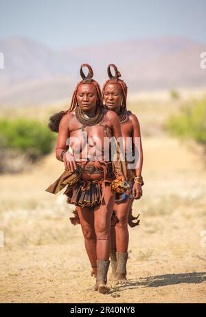 Zwei Frauen des Himba-Stammes laufen in Nationalkleidung durch die Wüste. Stockfoto