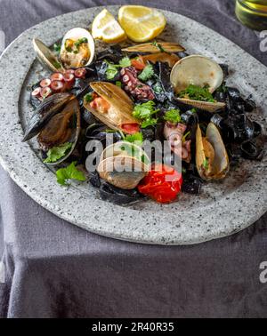 Meeresfrüchte schwarze Fettuccine fehttuchini. Schwarze Pasta mit Tintenfisch, Muscheln, Tintenfisch, Muscheln auf der Steinplatte. Gourmet Teller Stockfoto