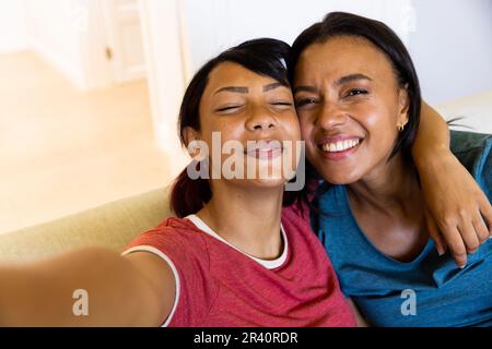 Porträt von glücklichen birassischen Schwestern, die in die Kamera schauen, Selfie machen, lächeln und umarmen Stockfoto