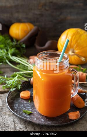 Frischer, natürlicher Mischsaft, gesundes Essen Konzept. Glasbecher mit frischem Karottensaft mit frischen Karotten und Kürbis auf Holzrost Stockfoto