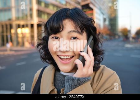 Portrait eines glücklichen koreanischen Mädchens, spricht mit dem Handy, sieht überrascht und glücklich aus, erhält positive tolle Nachrichten über Telefonverbindung Stockfoto