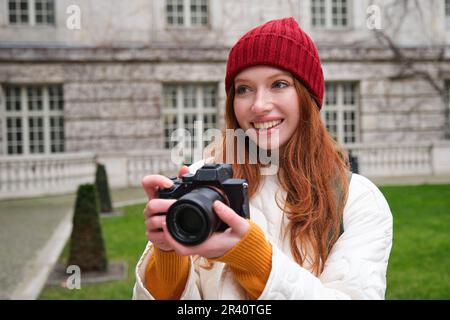 Glückliche Rothaarige Touristin, macht Fotos, Fotografin mit professioneller Kamera geht durch die Stadt und macht wunderschöne Fotos Stockfoto