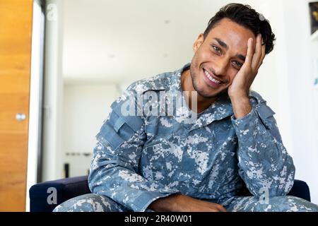 Ein glücklicher, birassistischer Soldat in Uniform, sitzt im Sessel und macht zu Hause Videoanrufe Stockfoto