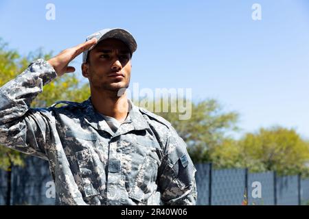 Ein birassischer Soldat, der Militäruniform trägt, draußen salutiert, mit Kopierraum Stockfoto