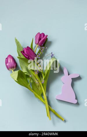 Lila Tulpen mit lila Kaninchen auf blauem Hintergrund. Konzept für Frühlings- und Osterferien. Draufsicht flach liegend. Speicherplatz kopieren. Stockfoto