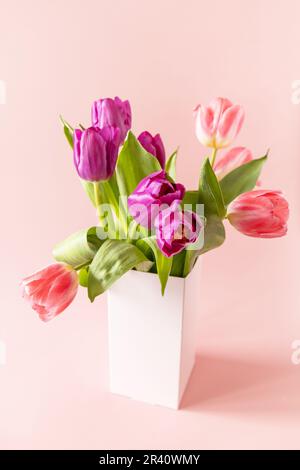 Bouquet von rosa und lila Tulpen mit bunten Wachteleiern auf rosa Hintergrund. Muttertag Urlaubskonzept. Stockfoto