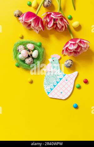 Farbenfroher Osterhintergrund. Weihnachtskarte mit bemalten Eiern, rosa Tulpe. Draufsicht flach liegend. Speicherplatz kopieren. Stockfoto
