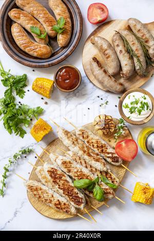 Grillmenü. Verschiedene gegrillte Würstchen mit frischen Kräutern und Gewürzen auf Marmortischplatte. Essen für Sommerpartys. Stockfoto