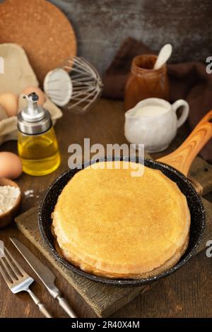 Wir feiern den Pfannkuchen-Tag, kochen ein gesundes Frühstück. Köstliche hausgemachte Crepes oder Pfannkuchen in einer Pfanne und Zutaten auf einem Stockfoto