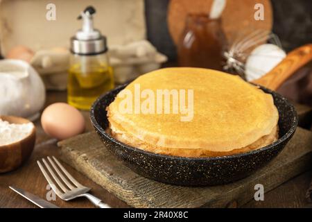 Wir feiern den Pfannkuchen-Tag, kochen ein gesundes Frühstück. Köstliche hausgemachte Crepes oder Pfannkuchen in einer Pfanne und Zutaten auf einem Stockfoto