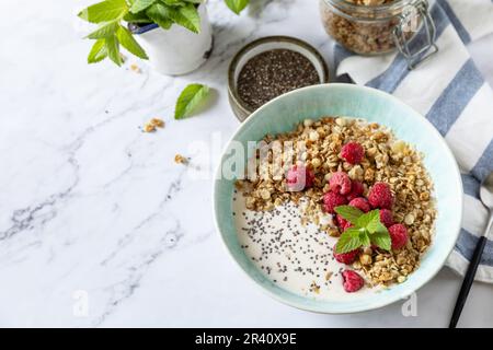 Frühstück, süßes Dessert. Ernährungskonzept. Hausgemachtes Müsli mit Joghurt, Chiasamen und Himbeere auf einem Marmortisch. C Stockfoto