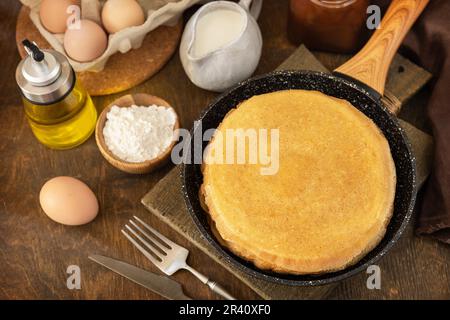 Wir feiern den Pfannkuchen-Tag, kochen ein gesundes Frühstück. Köstliche hausgemachte Crepes oder Pfannkuchen in einer Pfanne und Zutaten auf einem Stockfoto