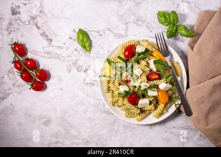 Frischer Pesto-Nudelsalat mit verschiedenen Farben von Kirschtomaten und Mozzarella mit hellem Hintergrund. Stockfoto