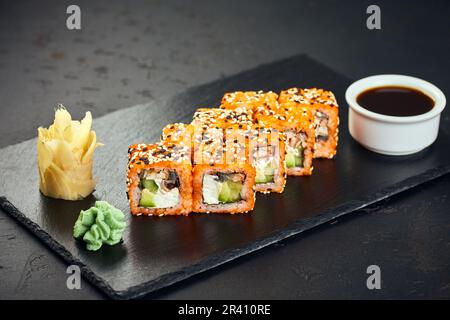 Rollen Sie mit Tobikokaviar, Sesamsamen, Lachs, Aal, Gurke, Avocado und Frischkäse auf dunklem Hintergrund. Sushi-Menü. Japanisch Stockfoto