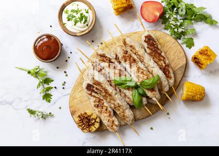 Sommerparty Essen. Grillgerichte. BBQ gegrillter Hähnchenkebab mit frischen Kräutern und Gewürzen auf Marmorplatte. Blick von oben. Stockfoto