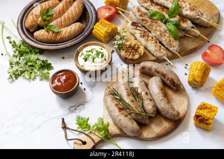 Grillmenü. Verschiedene gegrillte Würstchen mit frischen Kräutern und Gewürzen auf Marmortischplatte. Essen für Sommerpartys. Speicherplatz kopieren. Stockfoto