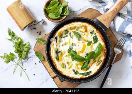 Spinat und Käseomelett. Frittata aus Eiern, Paprika und Spinat in einer Pfanne auf einer Marmorplatte. Blick von oben. Stockfoto