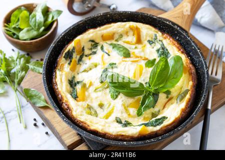 Spinat und Käseomelett. Frittata aus Eiern, Paprika und Spinat in einer Pfanne auf einer Marmorplatte. Stockfoto